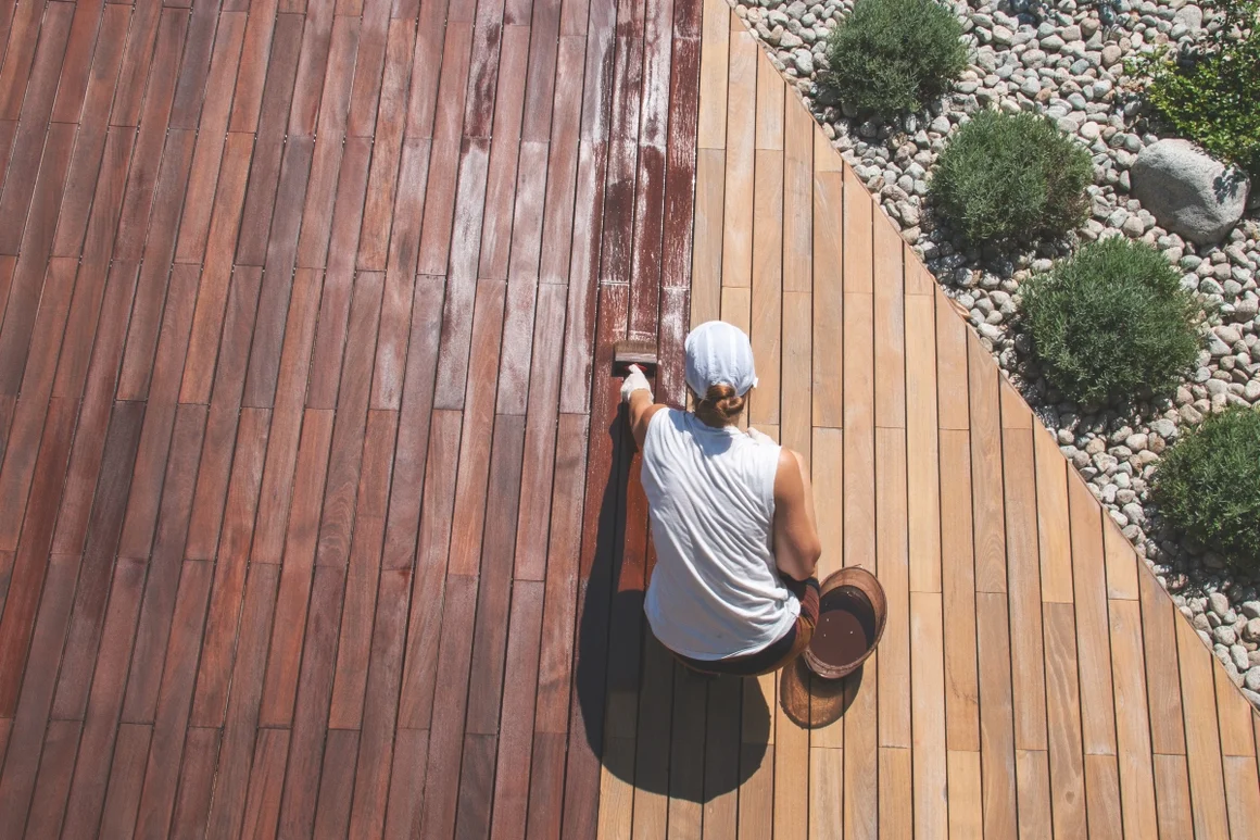 Person streicht Holzterrasse mit Pinsel